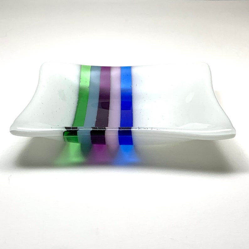May include: A white glass dish with a wavy edge and five colorful stripes in shades of green, blue, purple, and pink.