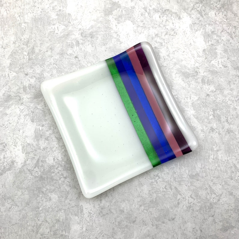 May include: A white square glass dish with a decorative stripe of green, blue, and purple.