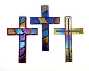 May include: Three stained glass crosses with different color patterns. The crosses are made of glass and have a metallic sheen. The crosses are hanging on a white background.