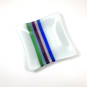 May include: A small, white square dish with a decorative stripe of blue, green, purple, and pink glass.