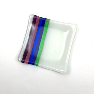 May include: A small, white square glass dish with a decorative stripe of green, blue, purple, and pink.