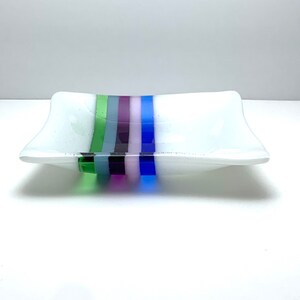 May include: A white rectangular glass dish with a decorative stripe design. The stripe design features green, blue, purple, and pink stripes.