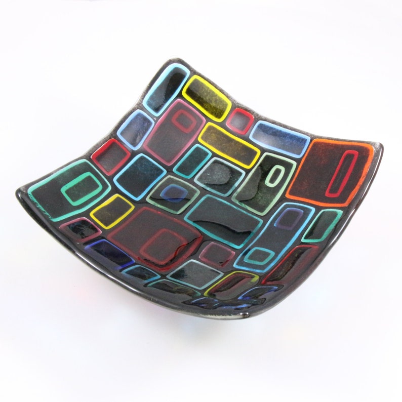 Puede incluir: Un plato cuadrado de vidrio con fondo negro y un patr&oacute;n geom&eacute;trico colorido de cuadrados y rect&aacute;ngulos. Los cuadrados y rect&aacute;ngulos est&aacute;n delineados en negro y rellenos de varios colores, incluidos rojo, amarillo, azul, verde y naranja.