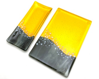May include: Two rectangular glass serving dishes with a black and yellow design. The larger dish is yellow with black and white accents. The smaller dish is yellow with black accents.
