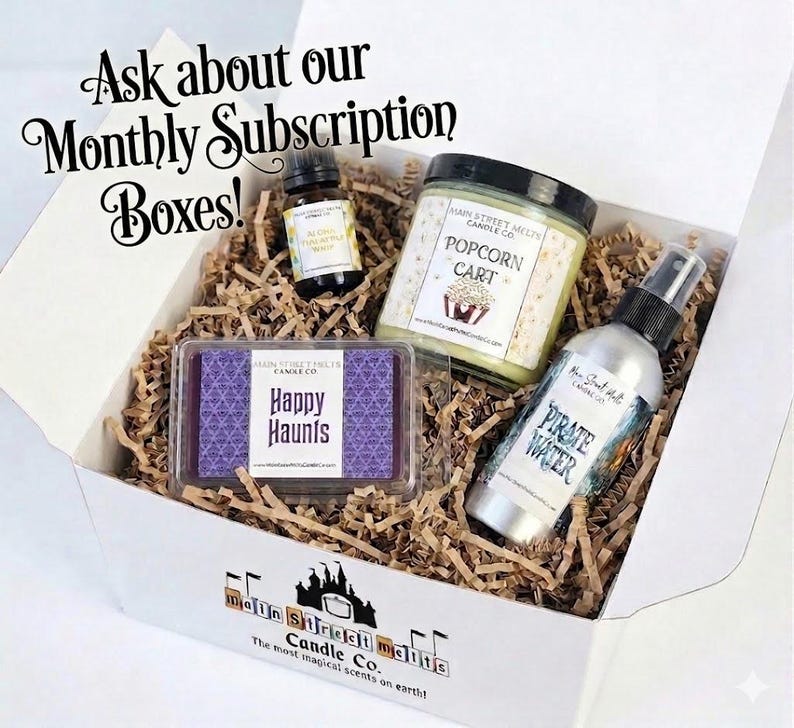 May include: A white gift box filled with brown paper crinkle filler containing a small amber glass bottle, a jar candle labelled Popcorn Cart, a rectangular wax melt labelled Happy Haunts, and a spray bottle labelled Pirate Water. Text reads Ask about our Monthly Subscription Boxes!