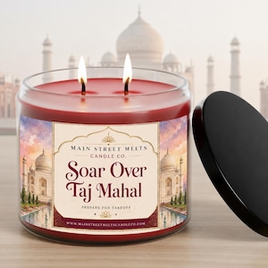 May include: A two-wick candle in a clear glass jar with red wax. The label features a watercolour illustration of the Taj Mahal and the text: Main Street Melts Candle Co. Soar Over Taj Mahal Prepare For Takeoff www.mainstreetmeltscandleco.com.