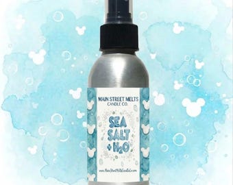 Könnte beinhalten: Eine silberne Metallsprühflasche mit schwarzem Sprühkopf. Das Etikett zeigt den Text Main Street Melts Candle Co. und Sea Salt + H2O vor einem hellblauen Aquarellhintergrund mit weißen kreisförmigen Blasen und Mausohr-Silhouetten.