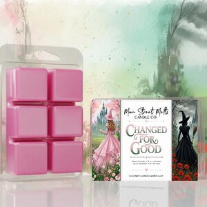 May include: A clear plastic clamshell container holding six pink wax melt cubes. The label features the text Main Street Melts Candle Co. Changed For Good, with illustrations of a person in a pink dress and a person in a black dress.