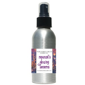 May include: A silver spray bottle with a black nozzle and cap. The label features the text "Rapunzel's Glowing Lanterns" with a castle illustration. The product is from Main Street Melts Candle Co.