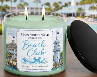 Könnte beinhalten: Eine hellgrüne Zwei-Docht-Kerze in einem Glasgefäß mit schwarzem Deckel. Das Etikett zeigt den Text Main Street Melts Candle Co. Beach Club, Green Clover + Crisp Aloe, eine Webadresse sowie Illustrationen eines Strandresorts und eines Leuchtturms.