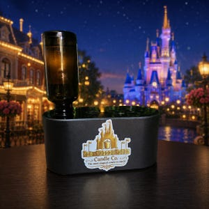 May include: A black electric wax warmer with a dark glass bottle attachment. The front features a white sticker with a gold castle illustration and the text MainStreetMelts Candle Co. The most magical scents on earth! in black lettering.