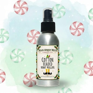 May include: A silver spray bottle with a black nozzle featuring a label that reads Main Street Melts Candle Co. Cotton Headed Ninny Muggins. The label includes a small green elf hat and yellow elf shoes with black curled toes on a white background.