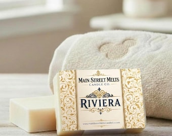 May include: A rectangular bar of off-white soap featuring a paper label with gold filigree patterns. The label displays the text Main Street Melts Candle Co. and the word RIVIERA in dark blue, along with the website address at the bottom.