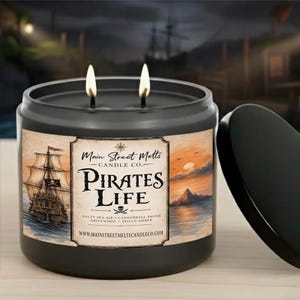 Peut inclure: Une bougie noire à deux mèches dans un pot avec une étiquette illustrant un voilier, un coucher de soleil sur l'eau et le texte Main Street Melts Candle Co. Pirates Life. L'étiquette mentionne aussi Salty Sea Air, Cannonball Smoke, Driftwood et Spiced Amber.