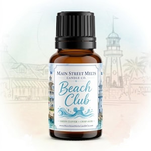 Könnte beinhalten: Eine kleine bernsteinfarbene Glasflasche mit schwarzem geripptem Verschluss. Das weiße Etikett zeigt den Text Main Street Melts Candle Co. Beach Club, Green Clover + Crisp Aloe und die Website. Das Etikett enthält Abbildungen eines Leuchtturms.
