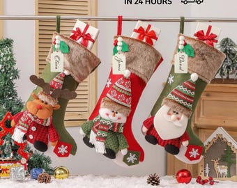 May include: Three Christmas stockings with personalized name tags and decorative figures of a reindeer, snowman, and Santa Claus. The stockings are red and green with faux fur trim and small gift boxes.
