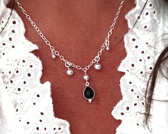 May include: A silver necklace with a black teardrop pendant and small silver beads hanging from the chain.