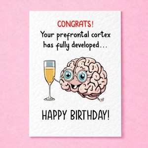 May include: A white greeting card featuring a cartoon brain wearing round glasses and holding a champagne flute. The text reads: CONGRATS! Your prefrontal cortex has fully developed... HAPPY BIRTHDAY! The design uses pink, black, and gold tones.