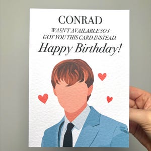 以下が含まれることがあります： 上部に「CONRAD」という名前が書かれた誕生日カード。テキストは「利用できなかったので、代わりにこのカードをあげました。お誕生日おめでとう！」と書かれています。青いスーツを着た人のイラストが下にあり、3つの赤いハートがあります。