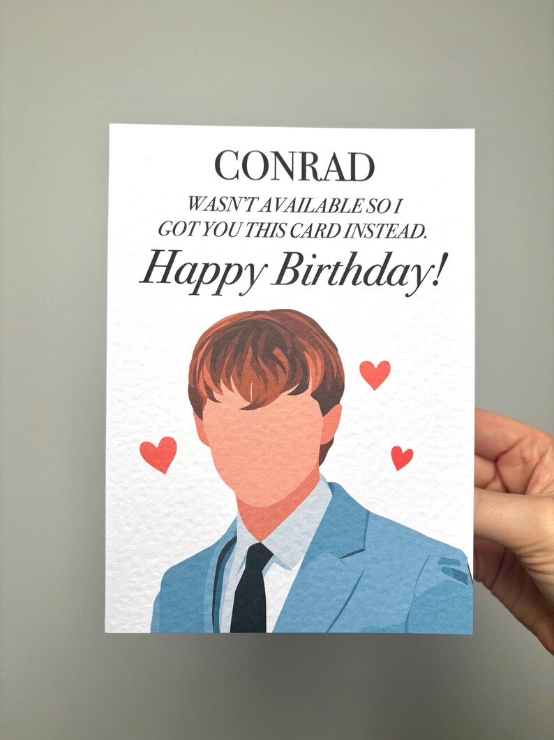 以下が含まれることがあります： 上部に「CONRAD」という名前が書かれた誕生日カード。テキストは「利用できなかったので、代わりにこのカードをあげました。お誕生日おめでとう！」と書かれています。青いスーツを着た人のイラストが下にあり、3つの赤いハートがあります。