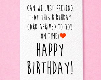 May include: A white rectangular birthday card with black handwritten-style text that reads: CAN WE JUST PRETEND THAT THIS BIRTHDAY CARD ARRIVED TO YOU ON TIME! followed by a small red heart, and the words HAPPY BIRTHDAY! in large black letters.
