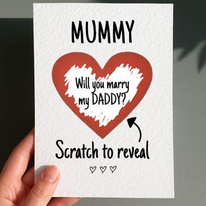 May include: A white card with the word "MUMMY" in black above a red heart. The heart contains the text "Will you marry my DADDY?" with an arrow pointing to "Scratch to reveal" below.