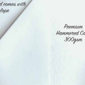 K&ouml;nnte beinhalten: Nahaufnahme einer wei&szlig;en, strukturierten Karte mit dem Text "Card comes with Envelope" und "Premium Hammered Card 300gsm". Die Karte hat eine subtile, geh&auml;mmerten Oberfl&auml;che.