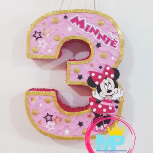 Puede incluir: Pi&ntilde;ata rosa con forma de n&uacute;mero 3 con borde de purpurina dorada, detalles de estrellas y puntos, y un gr&aacute;fico de Minnie Mouse. La palabra "Minnie" se muestra en la pi&ntilde;ata. Pi&ntilde;ata decorativa para una fiesta de cumplea&ntilde;os.