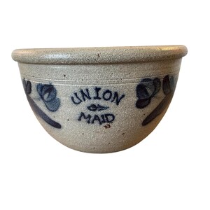 May include: A stoneware bowl with a light gray speckled finish. The bowl features blue floral designs and the words "UNION MAID" in blue lettering. The bowl has a rounded shape with a slightly flared rim.