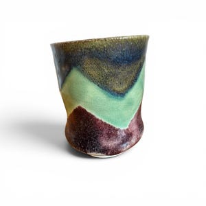 May include: A handmade ceramic cup with a unique, organic shape. The cup features a color palette of green, brown, and burgundy, with a glossy finish. The design has a chevron pattern. The cup is suitable for beverages.
