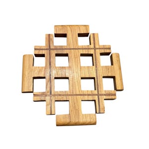 May include: A square, wooden trivet with a grid-like design. The trivet is made of light brown wood with a series of square cutouts. The design is geometric and modern, suitable for protecting surfaces from hot dishes.