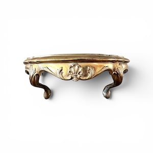 May include: A small, ornate, gold-colored table with a round top and three curved legs. The table has detailed carvings and a decorative floral design in the center. The table is likely made of wood.