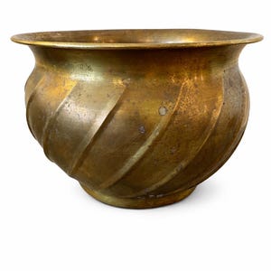 May include: A vintage brass planter with a spiral design. The planter has a wide, rounded body and a flared rim. The brass has a warm, aged patina, with subtle variations in color. The planter sits on a small, circular base.