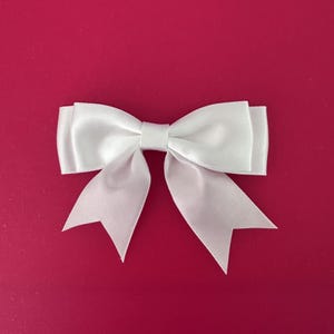 May include: A white satin bow against a vibrant red backdrop. The bow has a traditional shape, with a central knot and two V-shaped tails. This decorative bow is ideal for gift wrapping or craft projects.