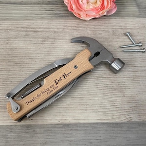 Pode incluir: Uma ferramenta multiusos com cabeça de martelo, alicates e outras ferramentas. O cabo é de madeira e tem a inscrição "Thanks for being my Best Man. From Tom".