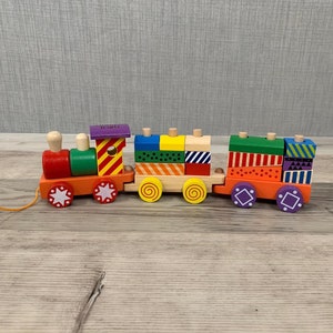 May include: A colourful wooden toy train with a pull string. The train has a locomotive and several carriages, each decorated with different geometric patterns and colours. The train is made of wood and has a natural finish.
