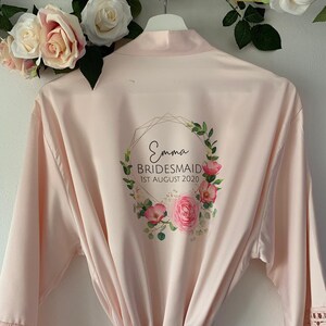 May include: A pale pink satin robe with a floral design and gold lettering. The text reads "Emma Bridesmaid 1st August 2020".