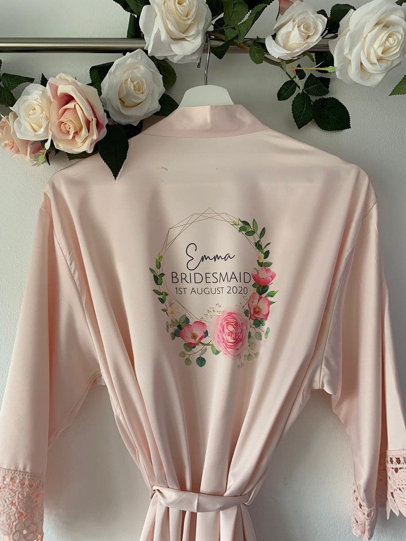 May include: A pale pink satin robe with a floral design and gold lettering. The text reads "Emma Bridesmaid 1st August 2020".