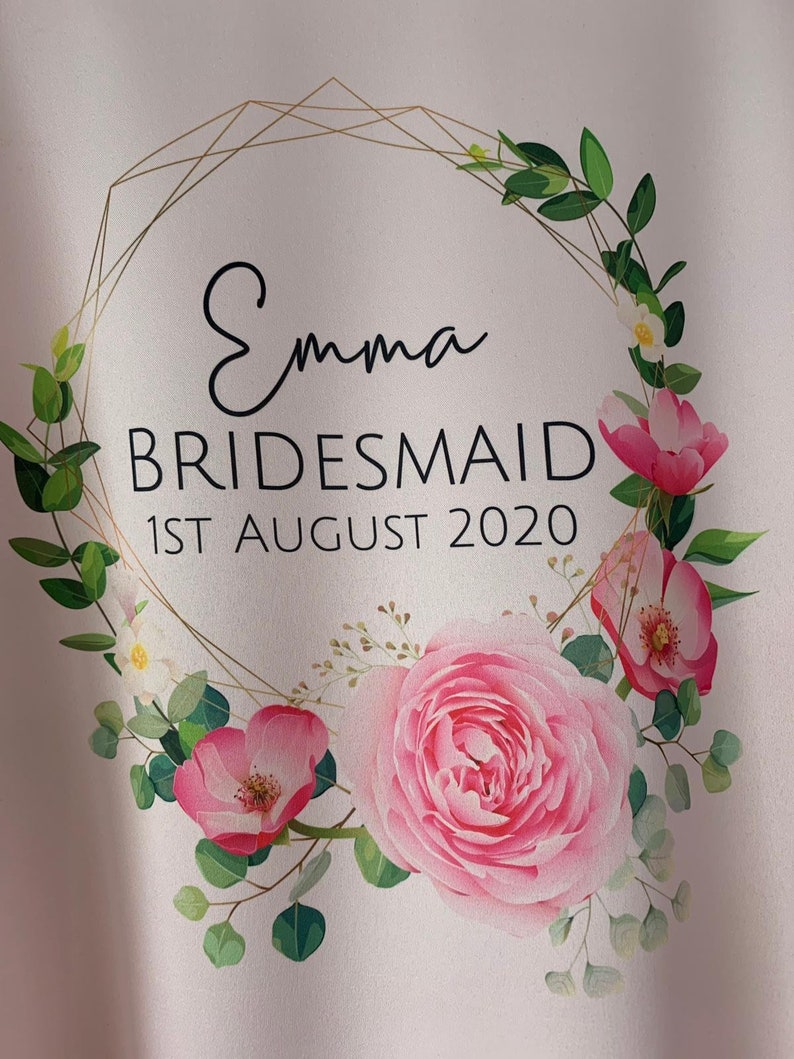May include: A white background with a gold geometric frame and pink flowers. The text "Emma Bridesmaid 1st August 2020" is inside the frame.