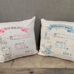 May include: Two white baby announcement pillows with pink and blue watercolor ribbons. The pillows feature a baby elephant illustration, birth details, and the names "Sarah Betty Jones" and "Bobby James Jones".