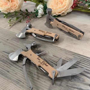 Può includere: Tre coltelli multifunzione tascabili con manici in legno. Ogni coltello ha un martello, un'ascia e altri strumenti. I manici sono incisi con nomi e date.
