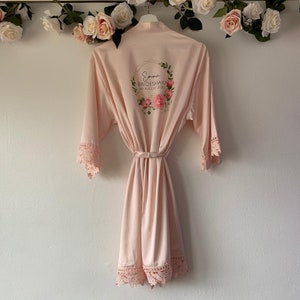 May include: A pale pink satin robe with lace trim and a floral design on the back. The design includes the text "Emma Bridesmaid 1st August 2020".