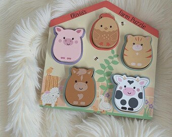 Peut inclure: Un puzzle en bois sur le thème de la ferme avec six formes d'animaux : un cochon, un poussin, un chat, un cheval, une vache et un mouton. Le puzzle est intitulé "Olivia's Farm Puzzle" et présente un toit rouge avec un fond jaune clair et des accents verts.