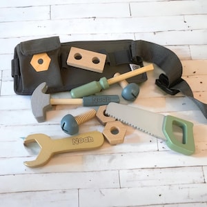 May include: A green and brown toy tool belt with a hammer, wrench, saw, screwdriver, and wooden blocks. The belt has the name "Noah" written on it.