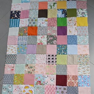 May include: A patchwork quilt composed of numerous fabric squares in various colors and patterns. The quilt features squares with unicorns, pandas, floral designs, and geometric shapes. The color palette includes pinks, blues, greens, and oranges.