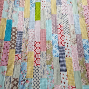 Könnte beinhalten: Ein Patchwork-Deckenstück mit verschiedenen floralen und geometrischen Mustern in Rosa-, Blau-, Grün-, Gelb- und Rottönen. Die Decke besteht aus Stoffresten, die in einem horizontalen Muster zusammengenäht wurden.