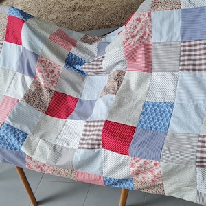May include: A patchwork quilt with squares of red, blue, and white fabric. The quilt is made of different patterns and textures, including floral prints, stripes, and polka dots.