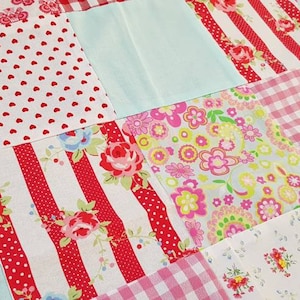 Könnte beinhalten: Eine Patchwork-Decke mit verschiedenen roten, weißen und rosa floralen Mustern. Die Decke besteht aus Quadraten aus verschiedenen Stoffen, die jeweils ein einzigartiges Design haben.