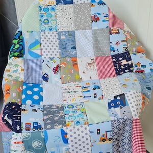 Könnte beinhalten: Eine Patchwork-Decke aus verschiedenen blauen, grauen und roten Stoffen mit unterschiedlichen Mustern. Die Decke zeigt eine Vielzahl von Designs, darunter Dinosaurier, Autos und geometrische Formen.