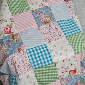 Könnte beinhalten: Eine Patchwork-Decke mit verschiedenen floralen und karierten Mustern in den Farben Rosa, Blau, Grün und Weiß.